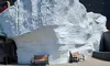 The image shows two benches on a sidewalk in front of a large white rock or iceberg-like structure with a building in the background.