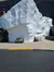 The image shows two benches on a sidewalk in front of a large white rock or iceberg-like structure with a building in the background.