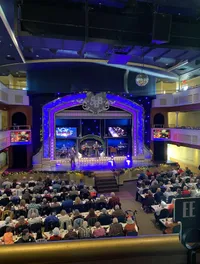 A live performance is taking place on a decorated stage in front of an audience seated at tables.