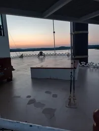 A calm, open deck overlooks a body of water and distant hills under a colorful sunset sky.