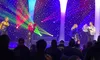 Performers in colorful, sparkling outfits are on stage with vibrant lighting effects and a starry backdrop, entertaining an audience.