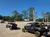 The image shows several off-road vehicles parked on a gravel lot with trees and a clear blue sky in the background.