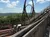 The image shows a wooden ramp leading to a roller coaster with a loop, set against a backdrop of trees and a clear blue sky.