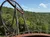 The image shows a looping roller coaster track set against a backdrop of lush green trees and a bright blue sky with clouds.