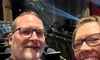 A smiling couple takes a selfie in a theater with a sign reading