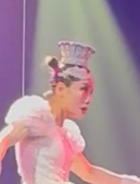 A performer balances on a unicycle atop a large ball while juggling, under colorful stage lights, as another performer looks on.
