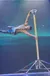 An acrobat is performing a horizontal hold on a vertical pole against a starry background.