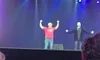 Two people are on stage, with one raising their arms triumphantly, while an audience watches.