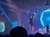 A person is performing an aerial acrobatic act on stage during a colorful concert or event.