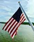 An American flag flutters on a pole by a body of water under a partly cloudy sky.