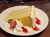 A slice of three-layer cake with cream frosting is served on a plate with strawberry sauce, whipped cream, and a strawberry garnish.