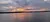 A serene lakescape at sunset, with glowing orange and pink hues reflecting on the water under a cloudy sky.