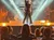 A performer strikes a dynamic pose on stage amidst bright lights and a rock band, with an audience watching intently.