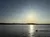 The image depicts a serene sunset over a calm body of water with a boat creating ripples in the foreground.