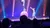 A performer balances on a unicycle atop a large ball while another person reaches toward them on a colorful stage with spotlights.