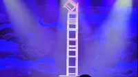 An acrobat is performing a balancing act on a tall stack of chairs, illuminated by colorful stage lights.