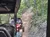 The image shows a person riding in a side-by-side vehicle on a rugged trail through a forested area.