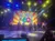 Performers are on stage in front of a colorful background that reads