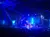A vibrant stage performance is taking place with blue lighting, featuring several performers in front of a large audience.