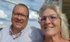 A smiling man and woman taking a selfie on a boat deck with a cloudy sky in the background.