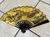 A decorative hand fan featuring intricate artwork and Chinese characters is displayed open on a tiled floor.