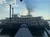 A large paddle steamboat is docked on calm water, with the sun casting dramatic rays behind a cloud in the sky.