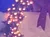 A group of performers in formal attire are singing on a festively decorated stage with Christmas trees and wreaths.
