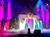 Three women in blue dresses perform on stage with Christmas decorations and colorful lighting.