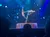 Two performers are balancing in an acrobatic pose on a circular platform with a blue, starry background.