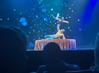 Two acrobats perform a balancing act on a stage with a starry backdrop.