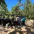Four people wearing casual clothes and masks are standing next to an off-road vehicle in a wooded area with a clear blue sky.