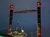 A boat with illuminated smokestacks is pictured against a dark evening sky, featuring decorative designs and a few people on the deck.