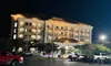 The image shows a brightly lit multi-story hotel at night with several cars parked in the foreground.