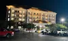 The image shows a brightly lit multi-story hotel at night with several cars parked in the foreground.