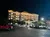 The image shows a brightly lit multi-story hotel at night with several cars parked in the foreground.