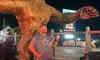 A man is posing with a green golf club in front of a large Bigfoot statue at night.