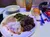 A plate of food featuring roast beef with gravy, mashed potatoes, green beans, and a chicken slice is served on a table alongside a roll with butter, an empty bowl, and a glass of iced tea.