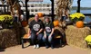 Two people are sitting on a bench surrounded by pumpkins and hay bales in front of a sign for the