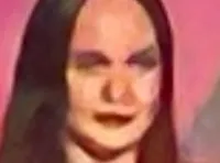 A performer on stage sings into a microphone, while four women in black dresses stand alongside, with a large image and the name 