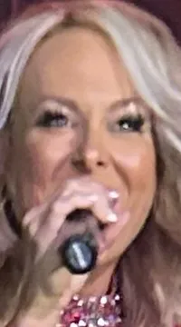 Two women in sparkly outfits perform on stage with a band in the background.