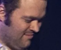 A band is performing on stage with three guitarists in front and a drummer in the background.