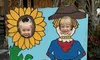 Two children are posing with their faces in cutouts of a sunflower and a scarecrow, next to a sign reading 