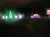 The image shows a nighttime scene with colorful light decorations, including a green tree, several reindeer, and a car.