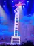 A performer balances acrobatically on a stack of chairs on stage under colorful lights.