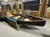 The image shows a wooden canoe displayed indoors, surrounded by fishing rods and equipment.