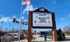 The image shows the entrance of a Veterans Memorial Museum with a large sign listing various wars, an American flag above, and a model airplane in the background.