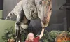 A person is posing with a life-sized dinosaur model, playfully holding its chin in a museum setting.