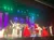 Performers in festive attire, including someone dressed as Santa Claus, are on stage during a colorful Christmas-themed show with decorations and vibrant lighting.