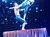 Two acrobats perform a balancing act on a small platform against a backdrop of blue and white lights.
