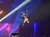 A musician is suspended upside down mid-air, playing a guitar with a crowd watching below.